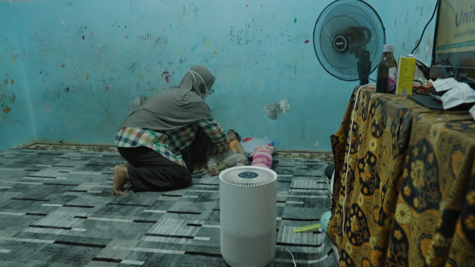 Mother Dianyra Eka Nastiti looking worried as she holds her child, with the smoke-filled sky visible in the background