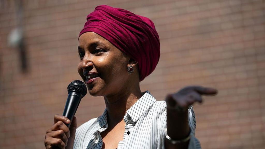 Congresswoman Ilhan Omar standing in front of a flag